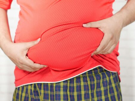 Close-up image of a man holding his bloated belly while wearing a red shirt. {{brizy_dc_image_alt entityId=